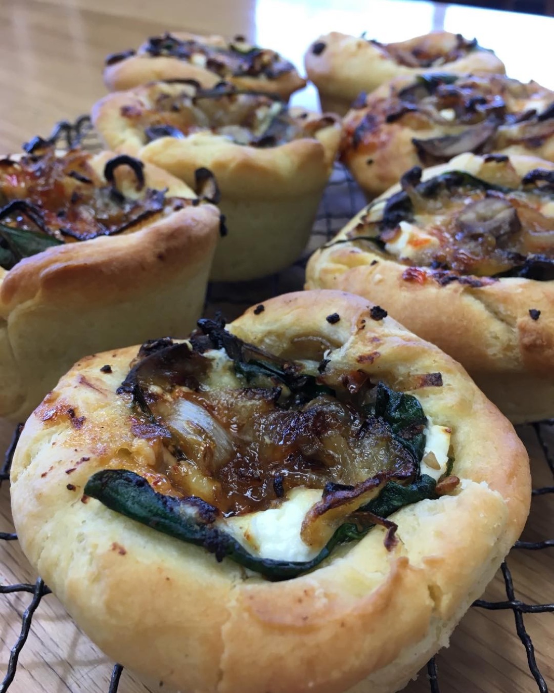 Small brioche tarts with caramelised onion and greens on a cooling rack