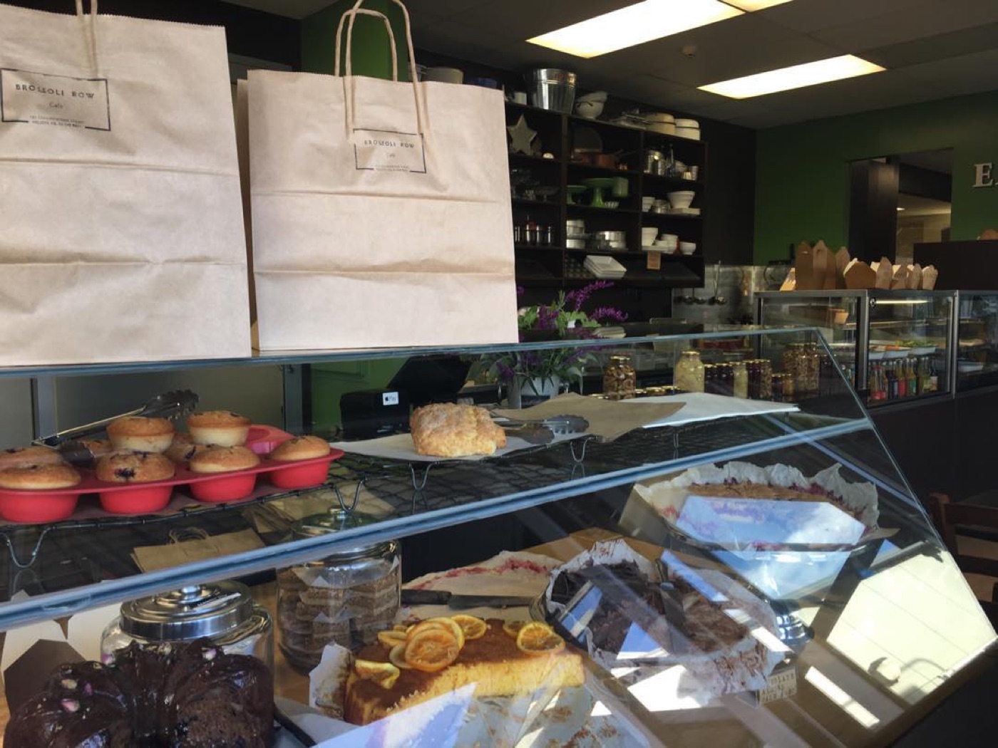 The Broccoli Row glass cabinet full of slices, tarts and cakes, with paper bags stacked on top