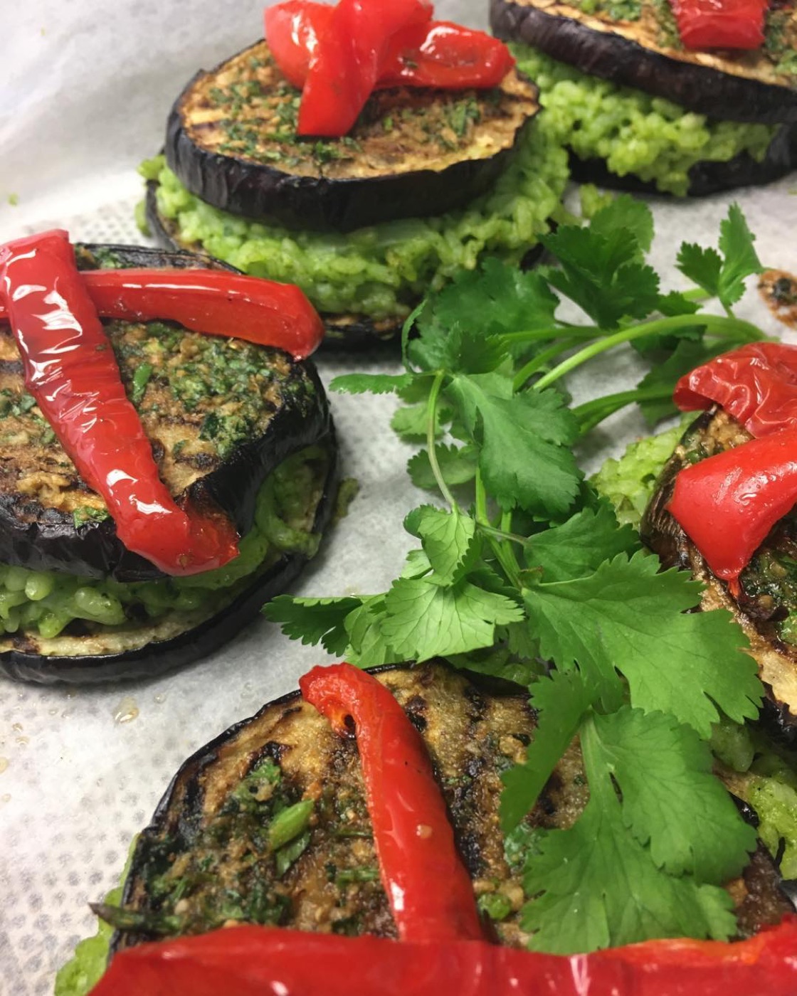 Grilled eggplant stacked with green rice, topped with roast red pepper and coriander