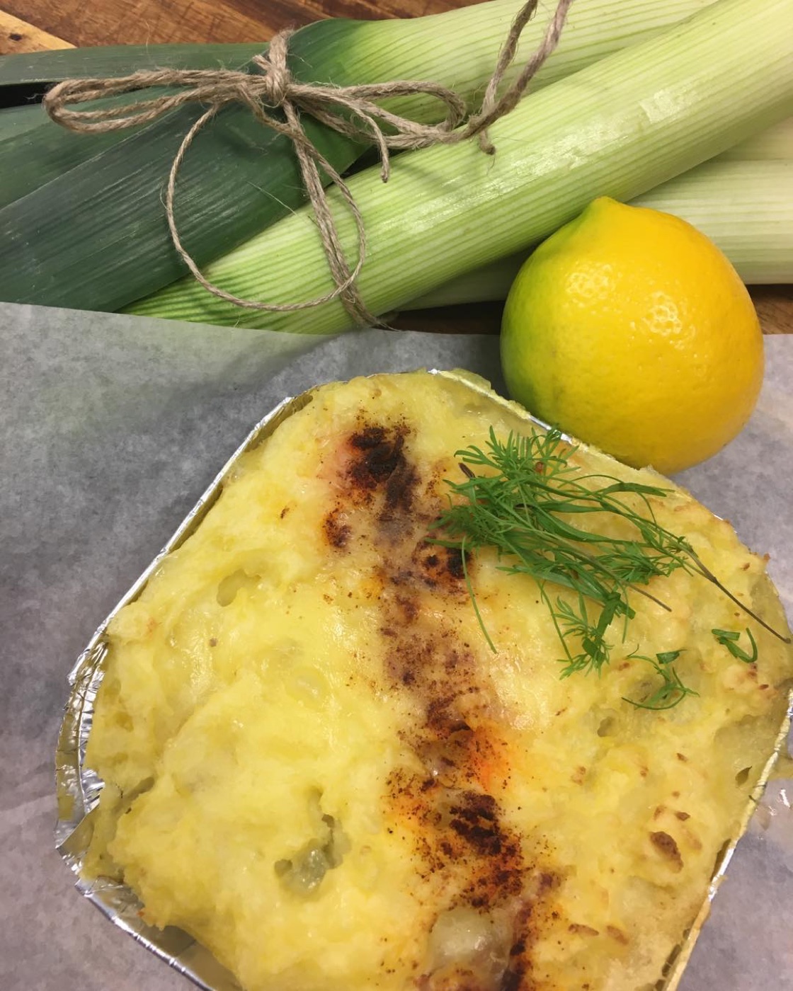 Golden fish pie in a foil dish beside a lemon and a leek