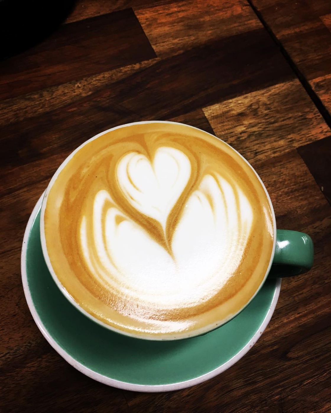 A heart latte in a green cup on a dark timber table