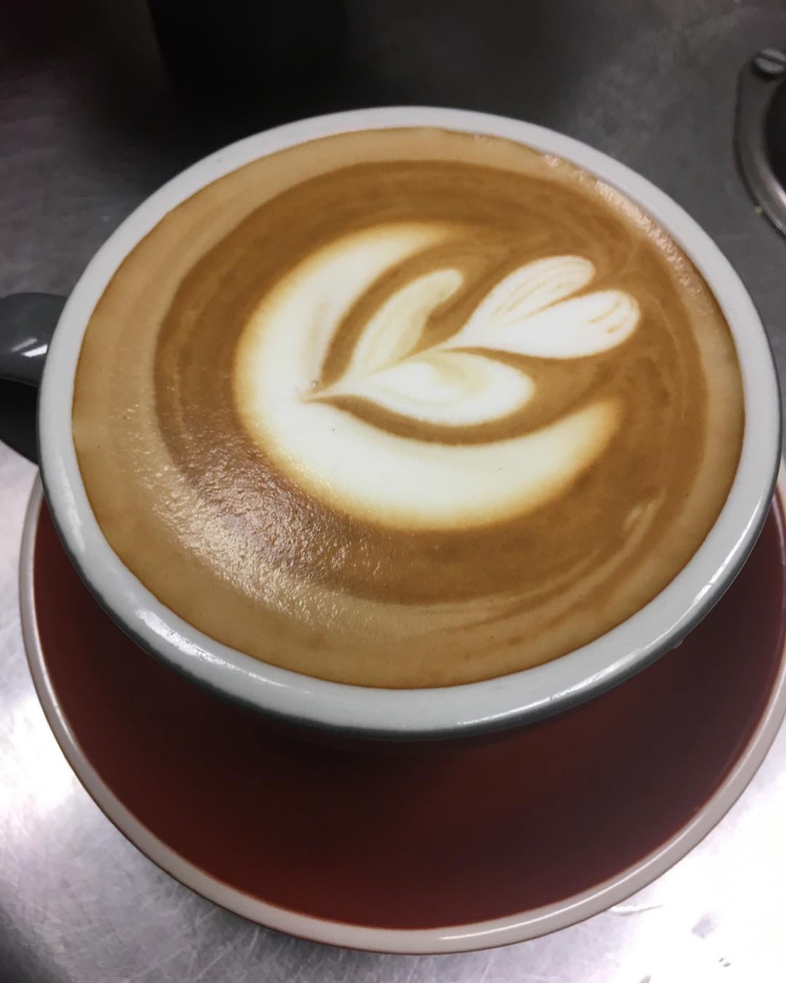 A tulip latte in a grey cup on a maroon saucer