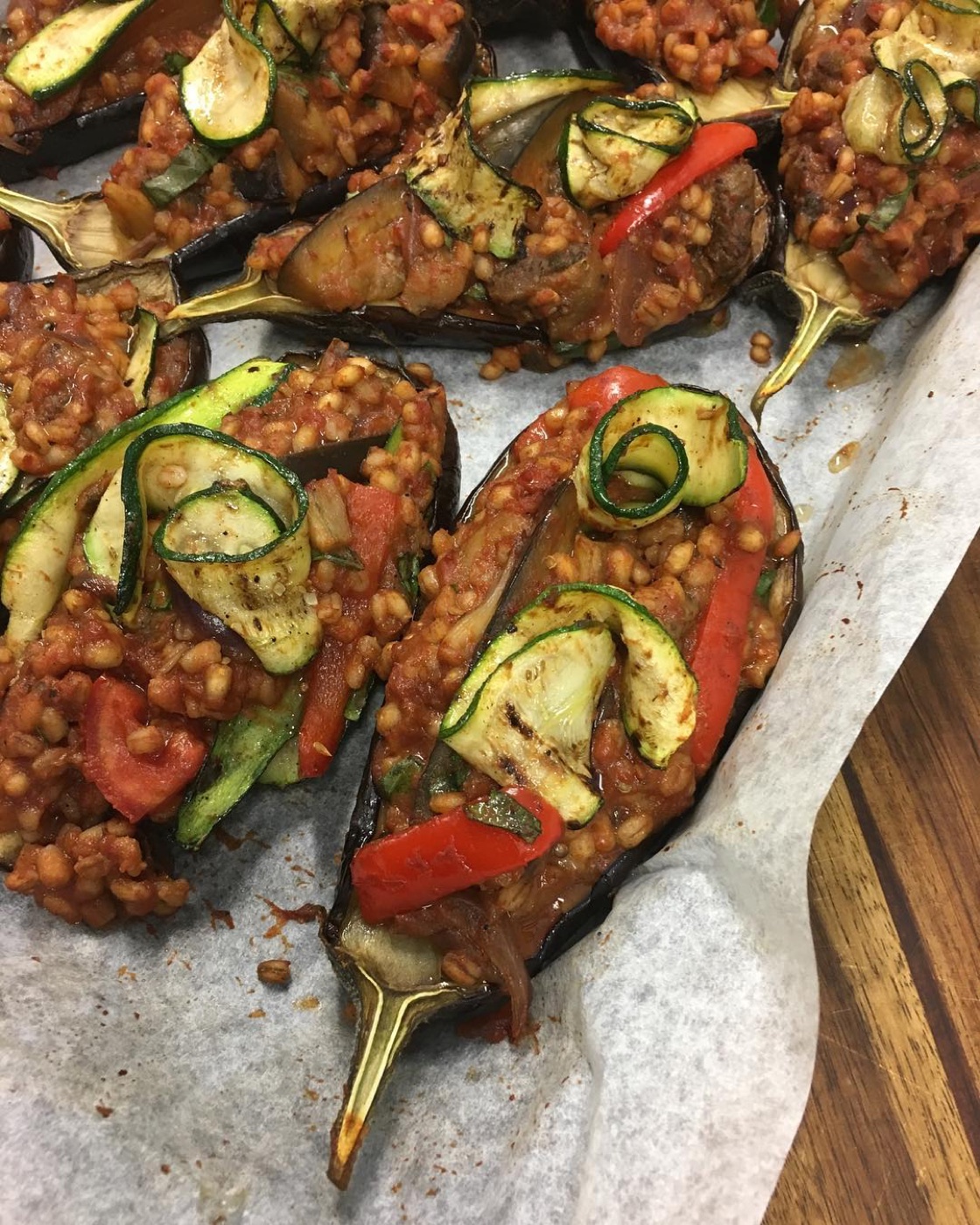 Roasted eggplant halves stuffed with grains, tomato and courgette