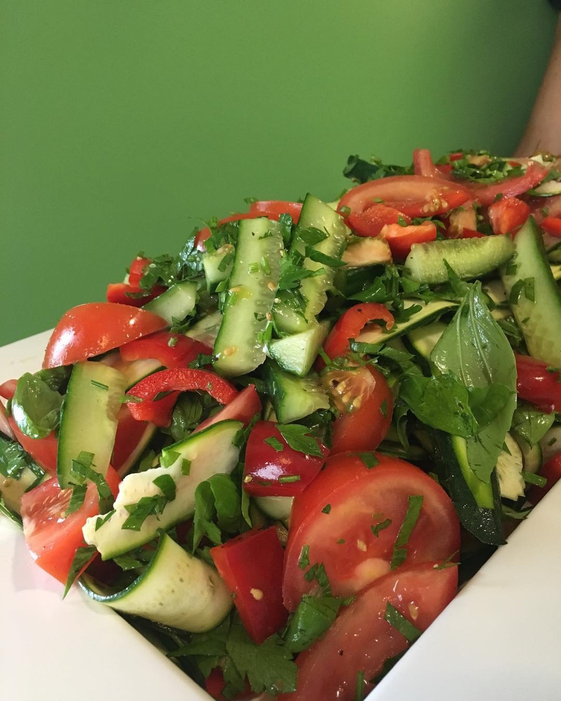 Summer salad of tomato, cucumber and herbs against the green wall of the cafe